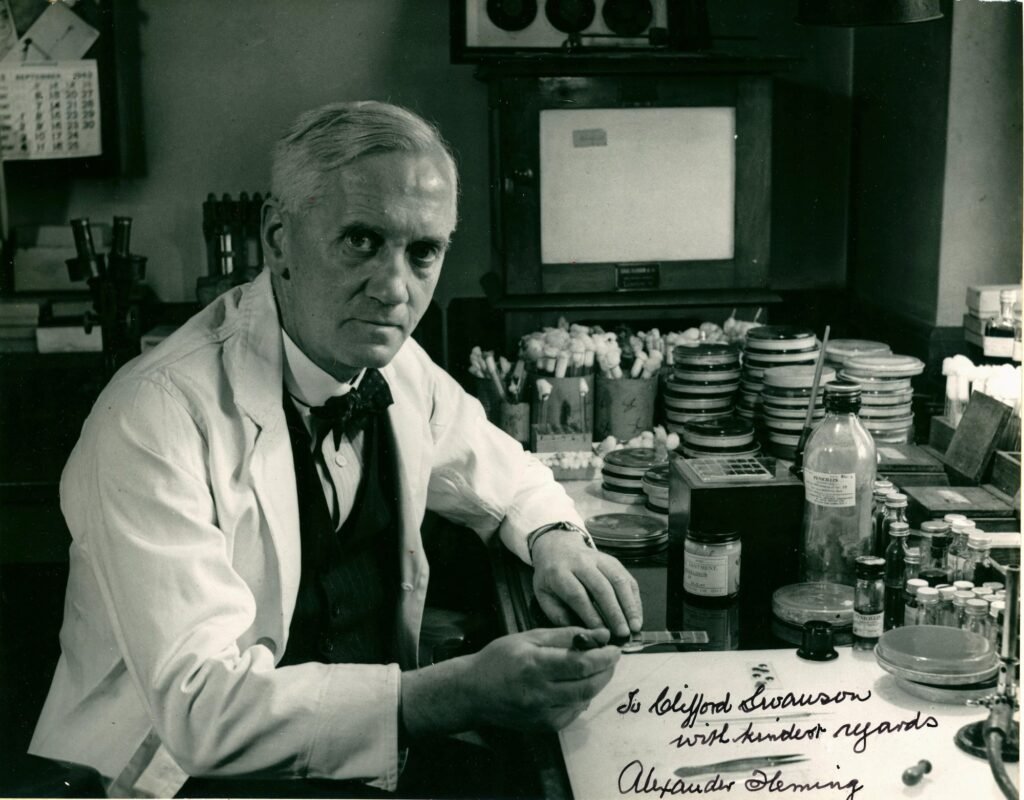 Alexander Fleming laboratuvar önlüğüyle masasında, çevresinde küf içeren petri kapları